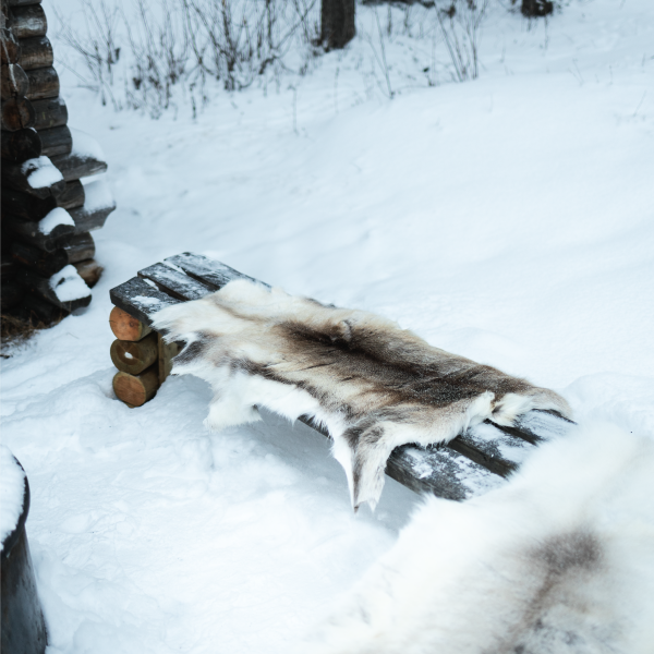  Reindeer hide draped over rustic wooden bench in snowy Lapland winter setting — lifestyle overhead view | Scandinavian gift